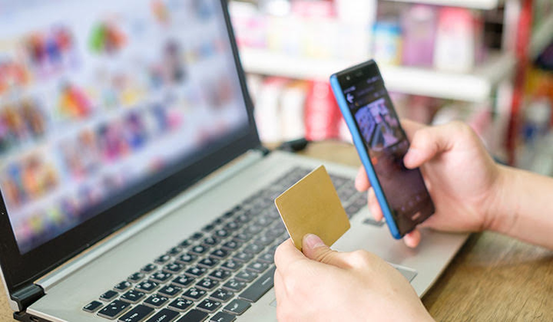 Een persoon heeft een laptop en telefoon bij zich en gebruikt een bankkaart om producten te kopen