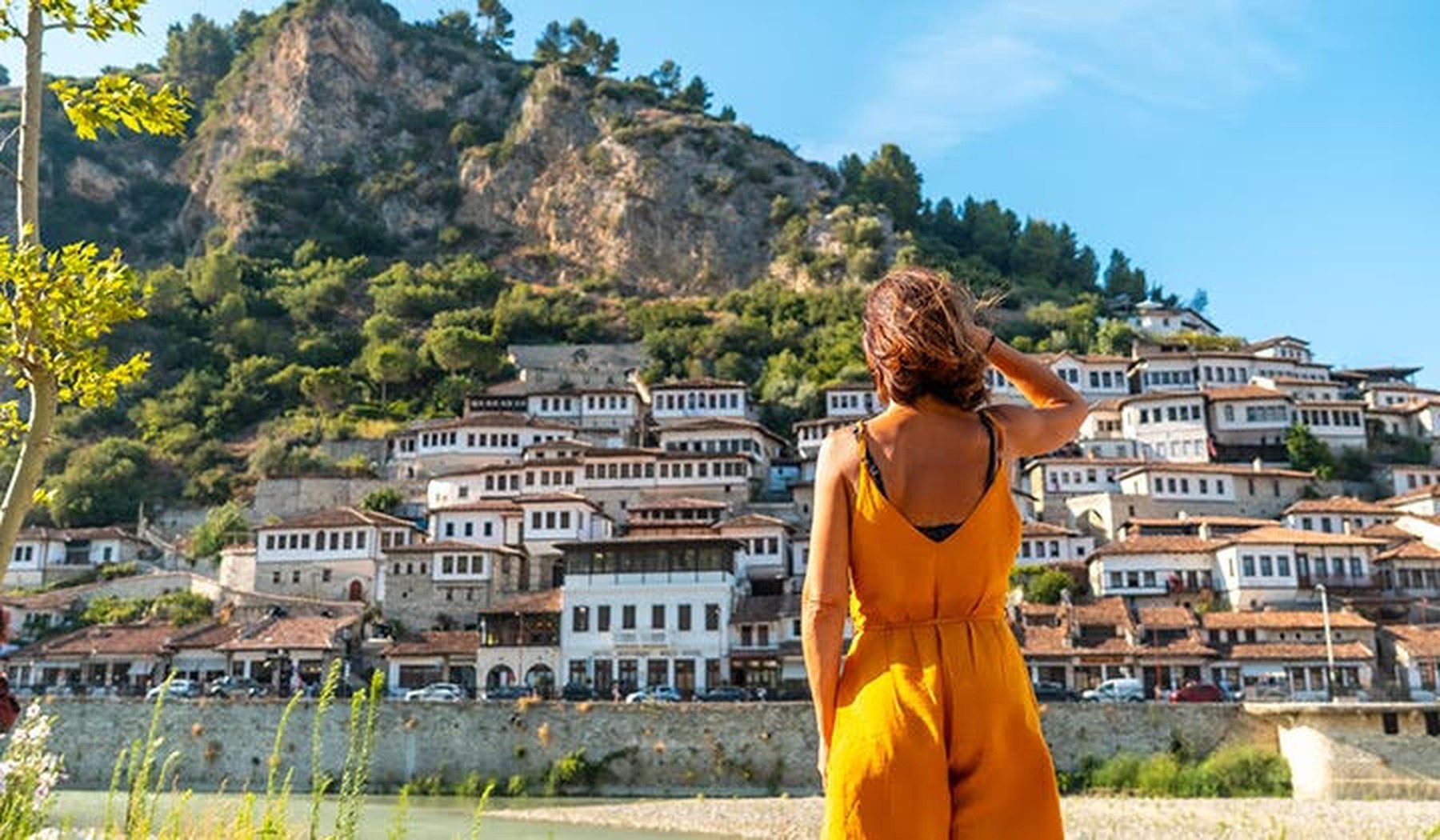 Een vrouw staat met haar rug naar de camera, met op de achtergrond een mooi, zonnig uitzicht over de natuur van Albanië