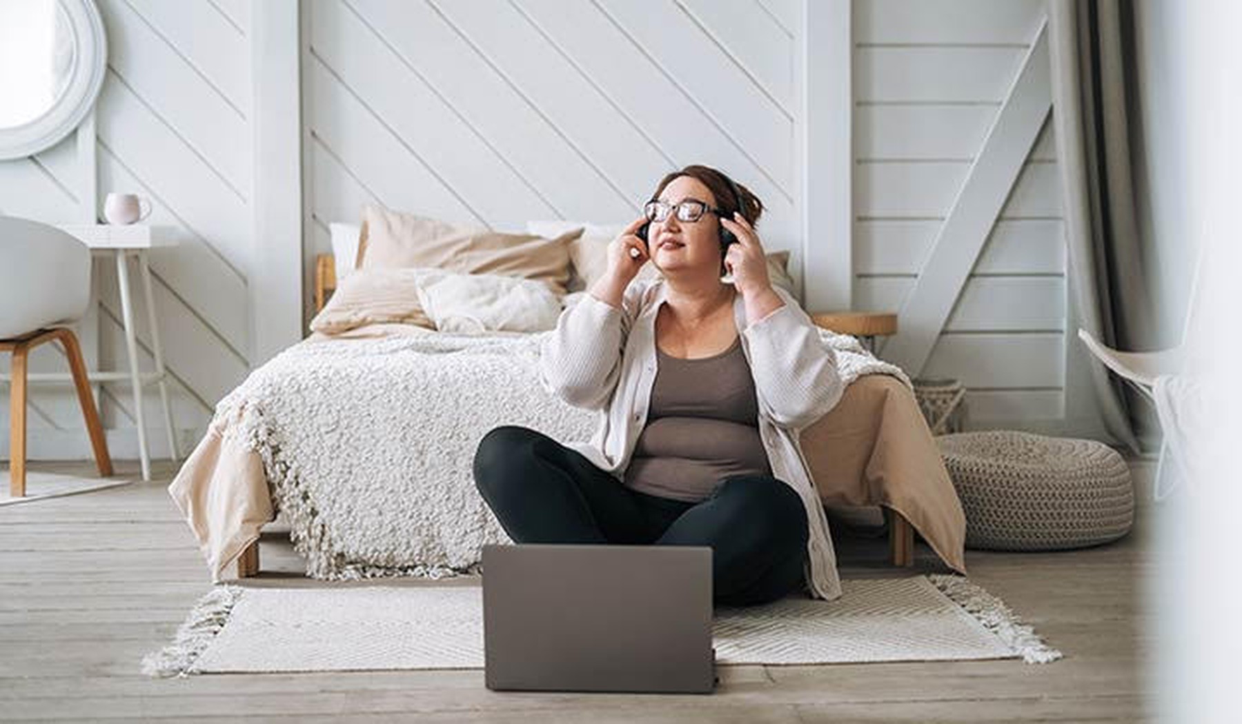 Een vrouw zittend op de grond met een koptelefoon op en een laptop voor haar