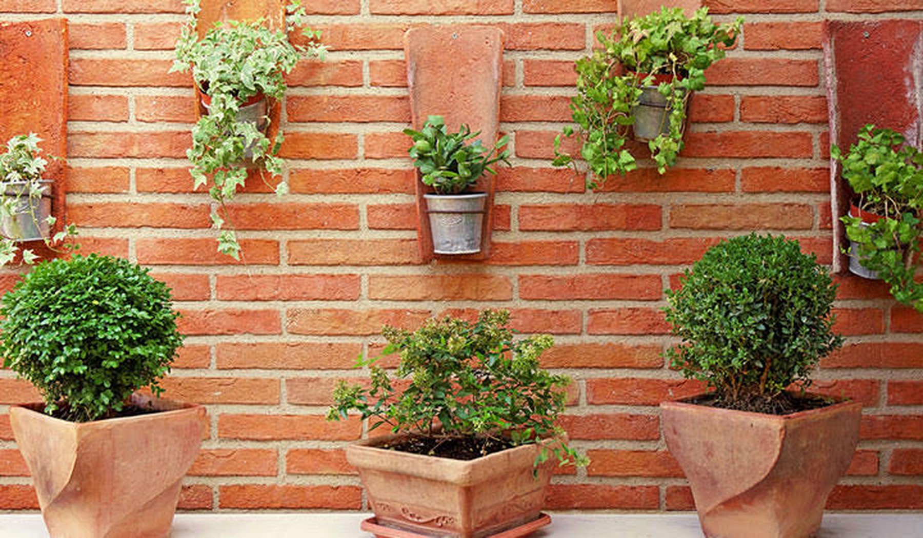 staande en hangende terracotta potten met planten op bakstenen muur