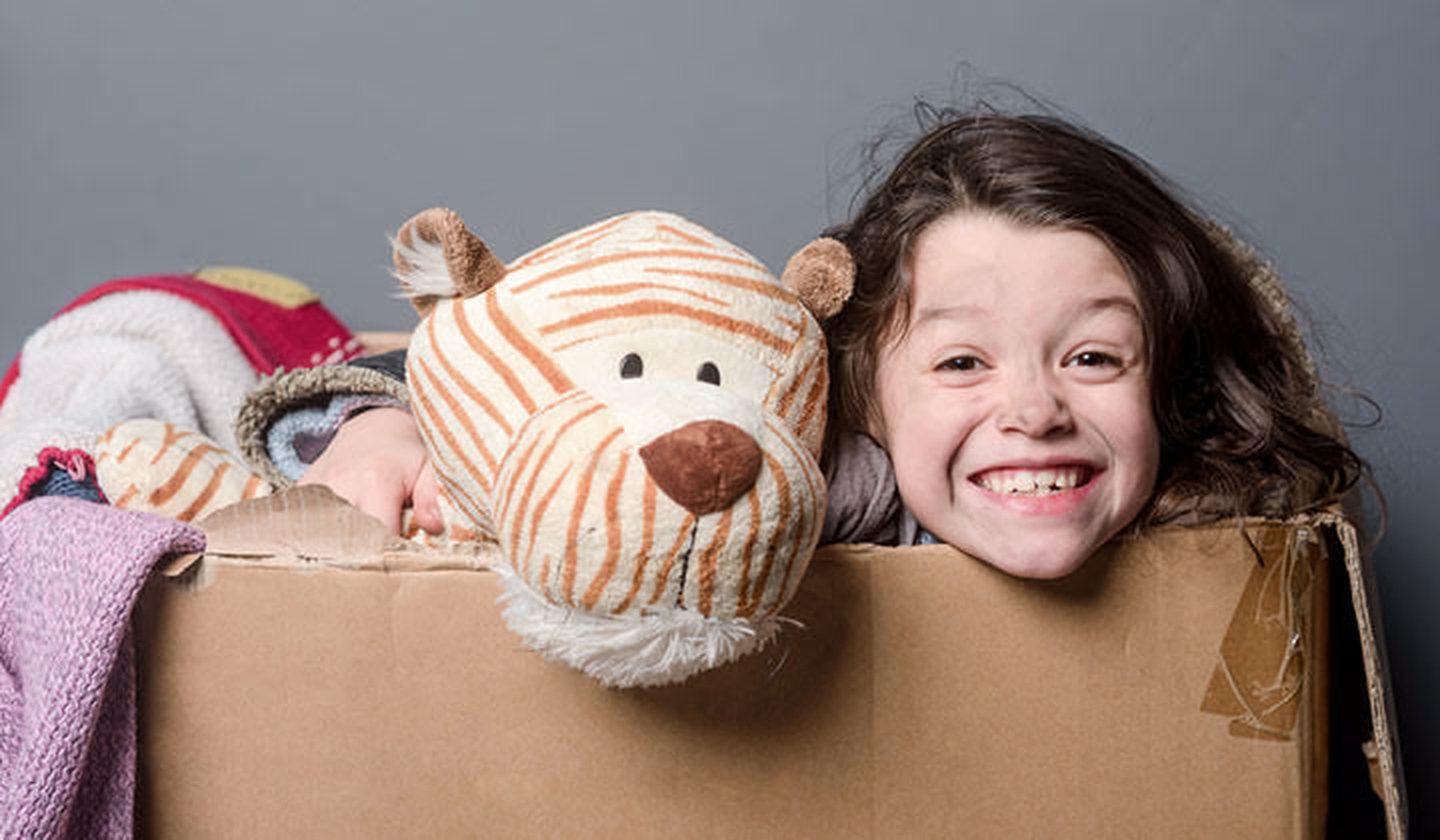 Een meisje met een grote knuffel tijger in een kartonnen doos