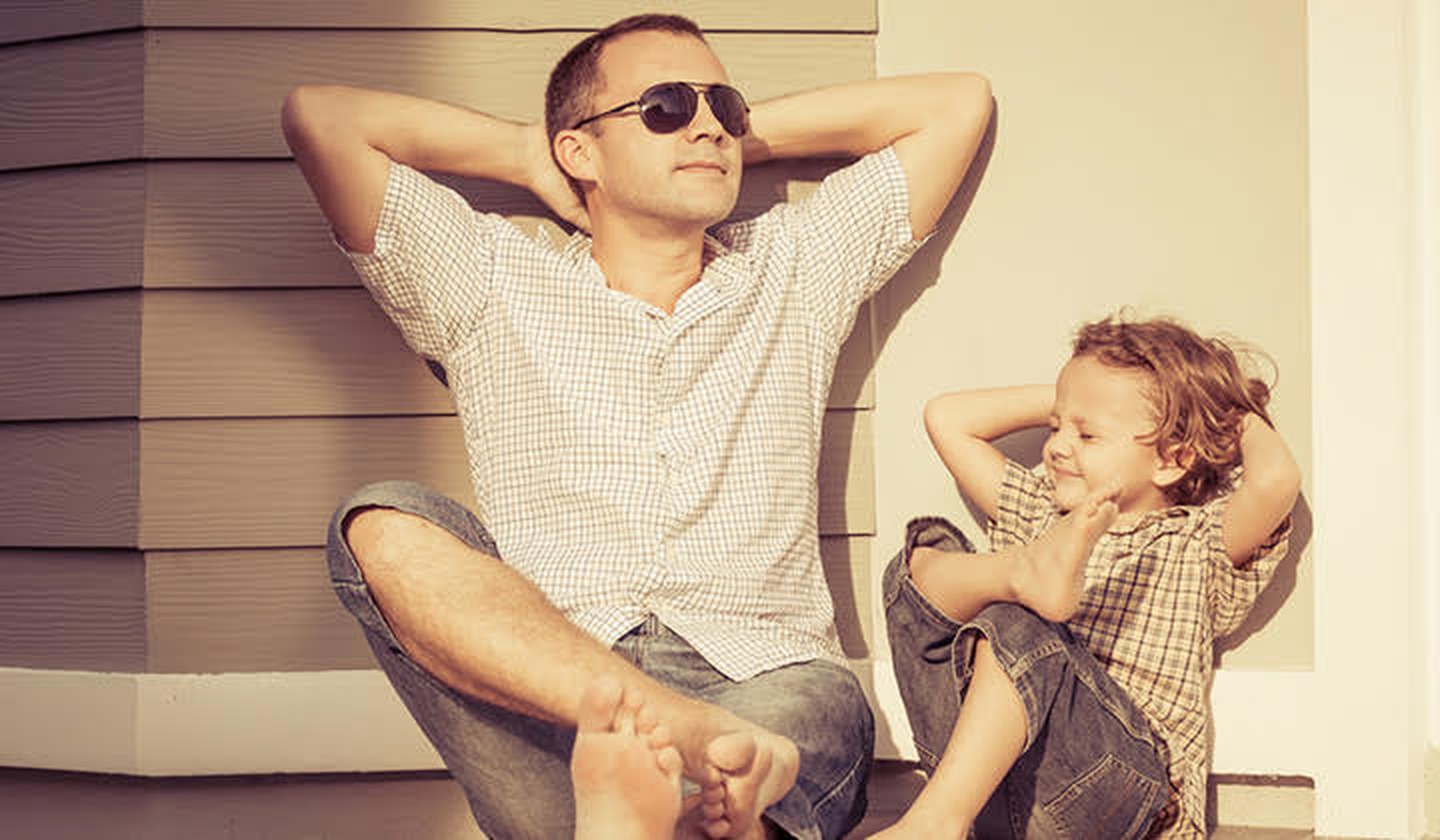 Een vader en zoon die tegen een muur aan relaxen in de zon