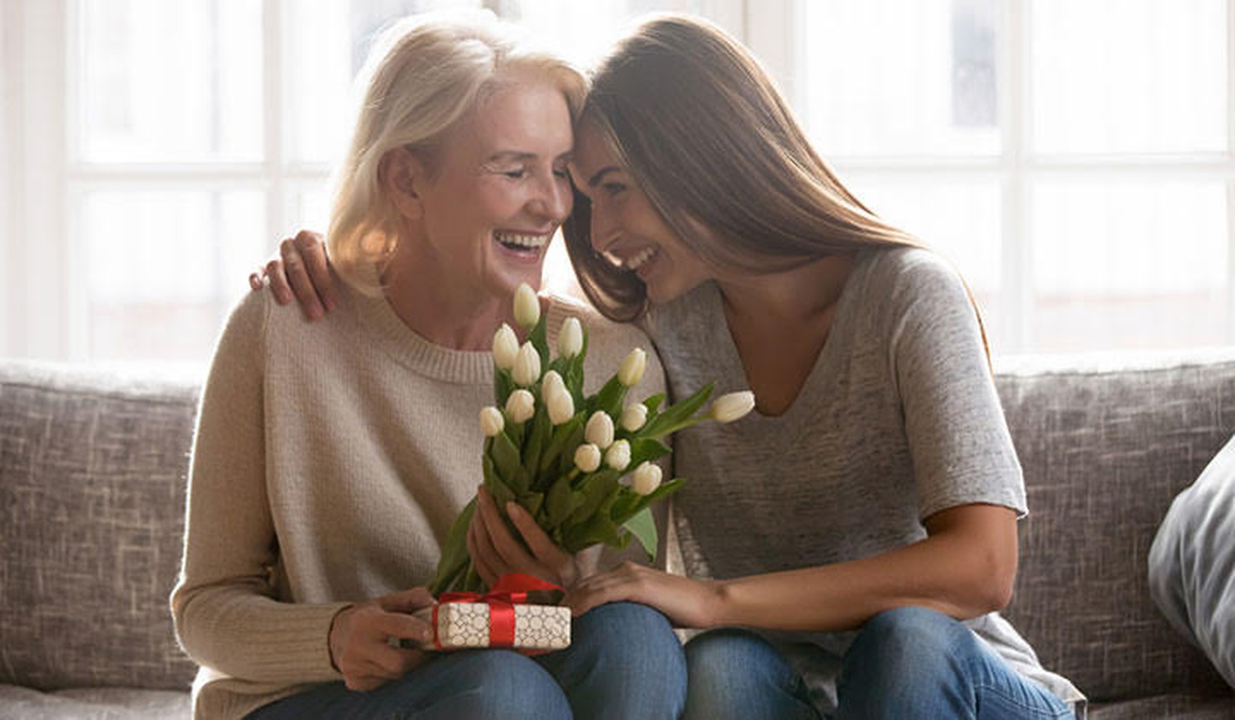 Een dochter die haar moeder op de bank een bos tulpen en ander cadeautje heeft gegeven