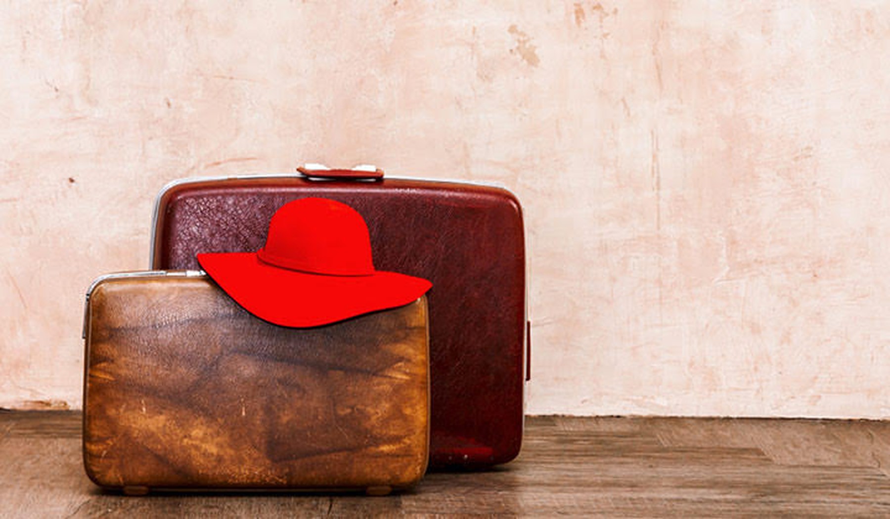 Twee vintage koffers met bovenop een rode hoed op de grond